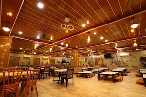 A restaurant with wooden ceiling beams, multiple tables and chairs, and wall murals. - Saavaj Resort (Talala)
