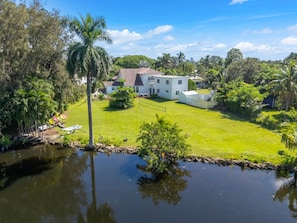 A large white house with a well-maintained lawn and a pond in the foreground. - Sprawling waterfront estate (Wilton Manors)