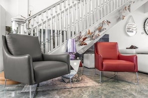 A modern living room with a staircase, two leather chairs, a white sofa, and a decorative wall piece. - Sprawling waterfront estate (Wilton Manors)