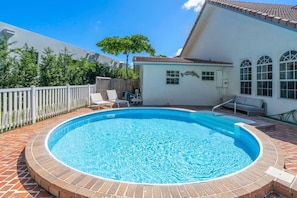 A swimming pool with a brick border, surrounded by a white fence, and a building with a tiled roof in the background. - Sprawling waterfront estate (Wilton Manors)