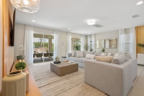 A modern living room with a sofa, coffee table, and a TV mounted on the wall. - 10br Near Disney Private Pool, spa & Game Room (Kissimmee)