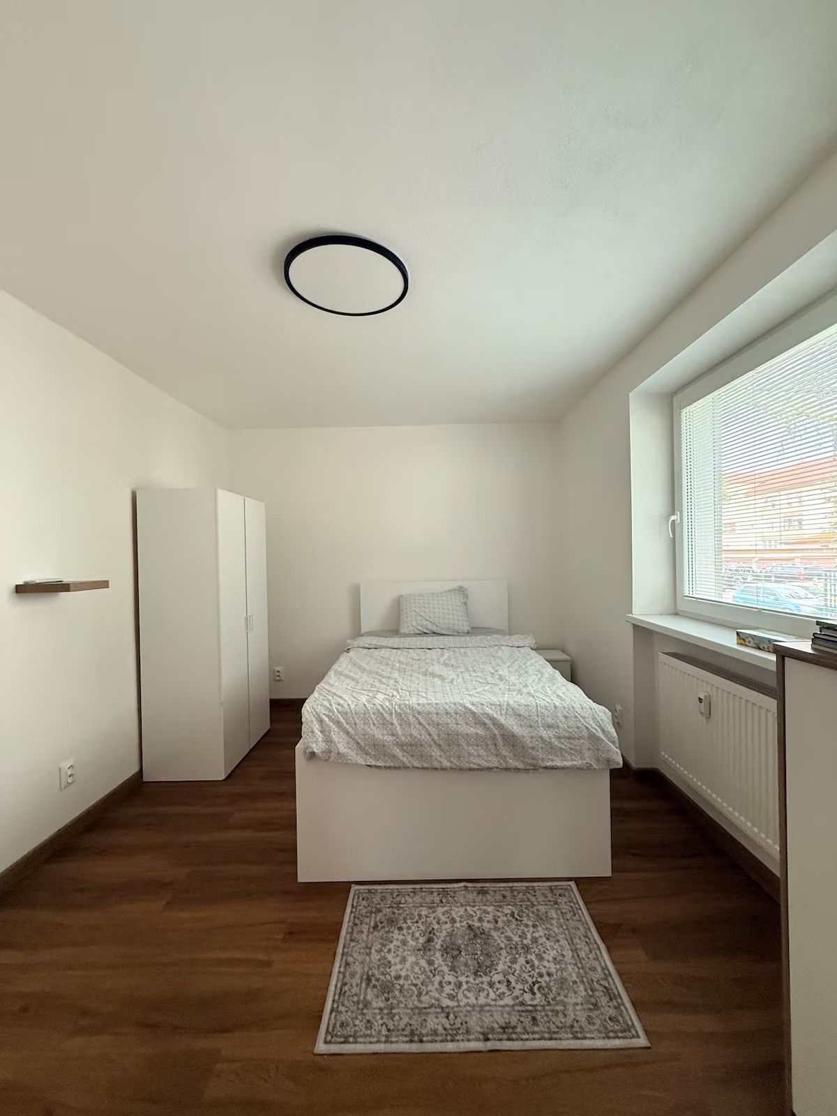 Una camera da letto con un letto, una finestra con persiane, un termosifone e una porta.