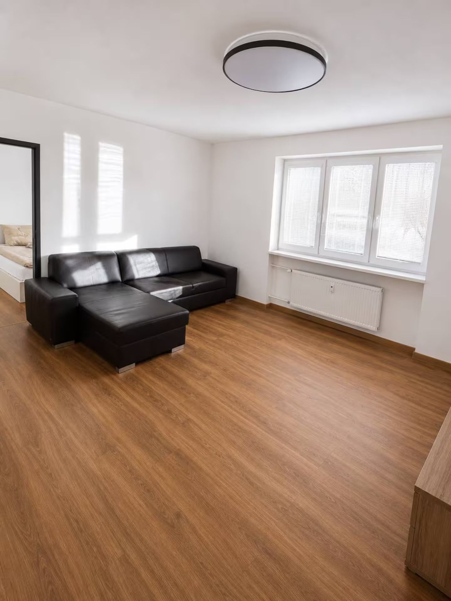 En moderne stue med en modulsofa, et rundt sofabord og et stort vindue med persienner.