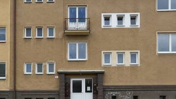 Ein mehrstöckiges Gebäude mit einer glatten Fassade, einem zentralen Eingang mit einer Tür und einem kleinen Balkon im zweiten Stock.