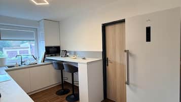 A modern kitchen with a built-in island, a refrigerator, and a window with blinds.