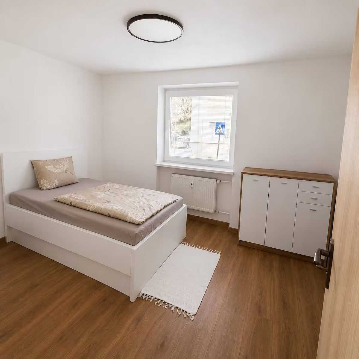 Ein Schlafzimmer mit Bett, Fenster, Heizkörper und Kleiderschrank.