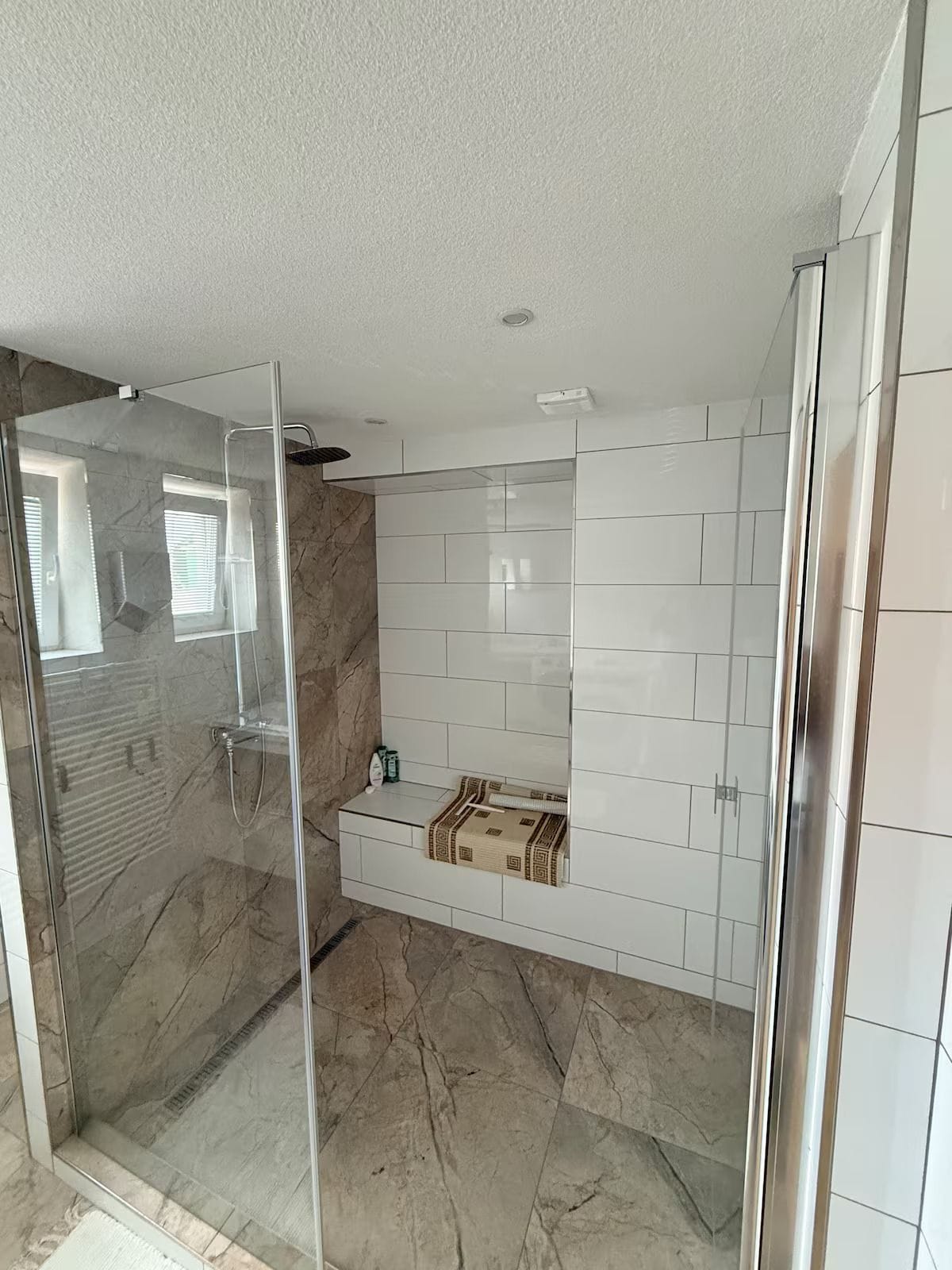 Et moderne badeværelse med en glasvæg omkring brusebadet, hvide flisevægge og et marmorgulv.