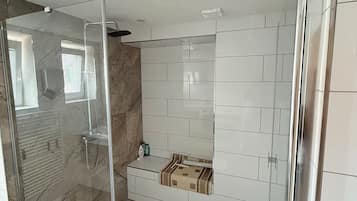 A modern bathroom with a glass-enclosed shower, white tiled walls, and a marble floor.