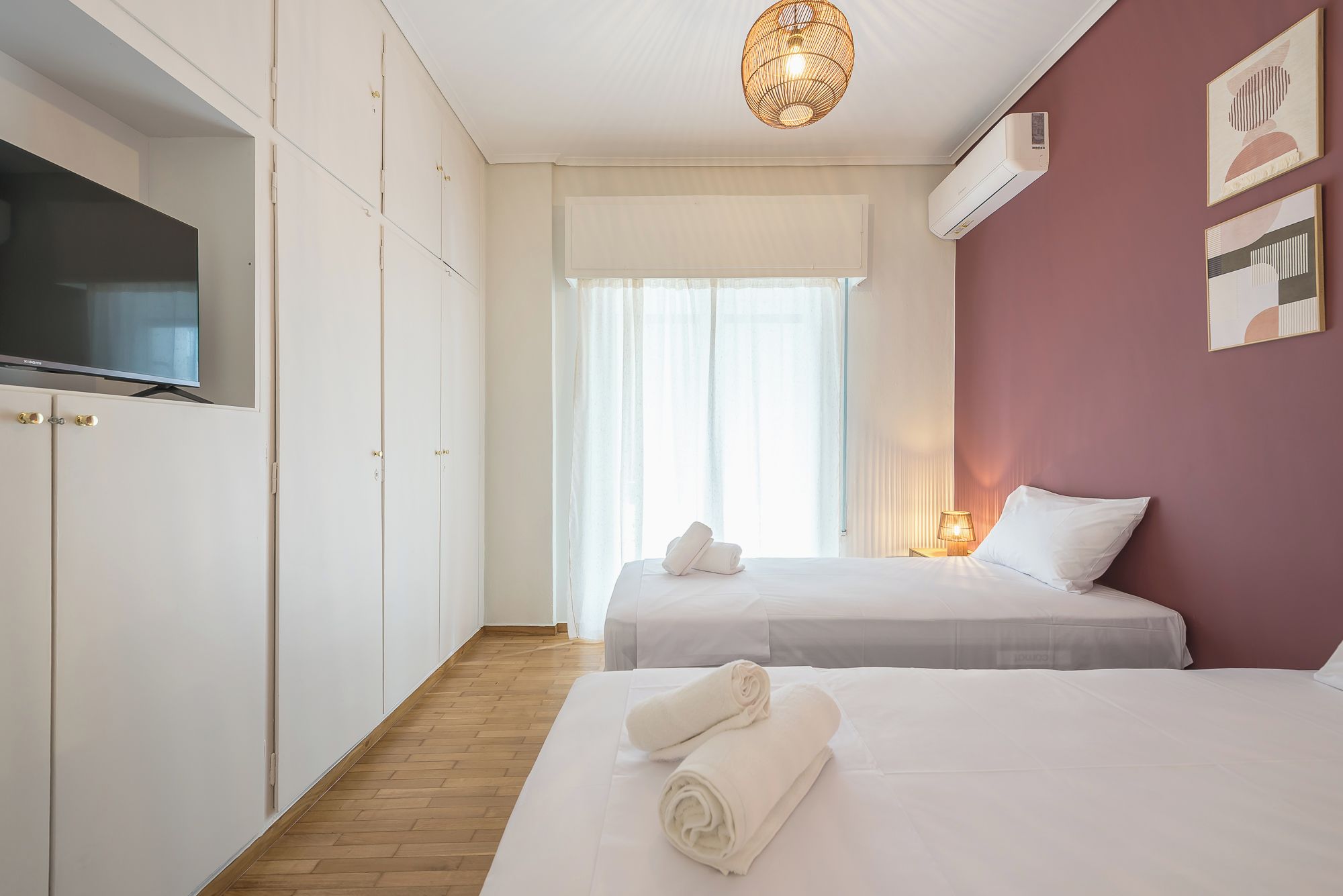 A hotel room with two beds, a television, and a wall-mounted air conditioner.
