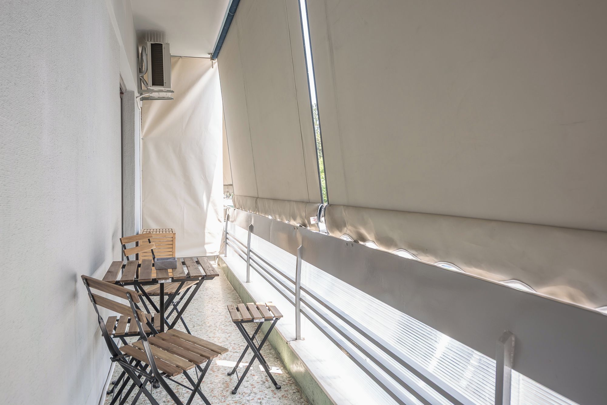 A balcony with a table and chairs, a white curtain, and a window with blinds.