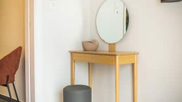 A room with a wooden console table, a round mirror, a small stool, and a brown chair.