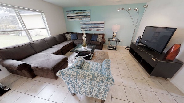 A living room with a sectional sofa, a coffee table, a TV stand, and a lamp. - 4BR Home in Kissimmee Mickey & Minnie Room (Kissimmee)