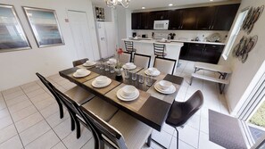 A modern kitchen with dark cabinets, a white countertop, and a dining area with a long table set for six. - 4BR Home in Kissimmee Mickey & Minnie Room (Kissimmee)