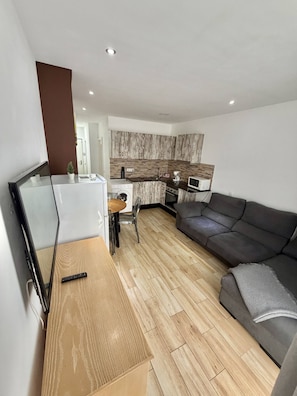 A modern living room with a grey sofa, wooden flooring, and a kitchen area with wooden cabinets and appliances. - 403|Apartment with ocean views|Canteras Beach (Las Palmas de Gran Canaria)