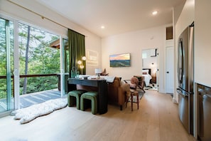 A modern kitchen with a dining area, a large window with a view of trees, and a refrigerator. - Birch & Beard | Boutique Forest Stay + Hot Tub (Young Harris)