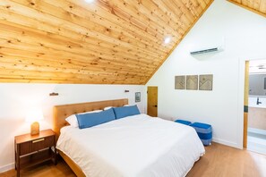 Ein Schlafzimmer mit schrägen Wänden, einem Bett mit weißer und blauer Bettwäsche, einem Nachttisch mit einer Lampe und einem kleinen Nachttisch mit einem Buch.