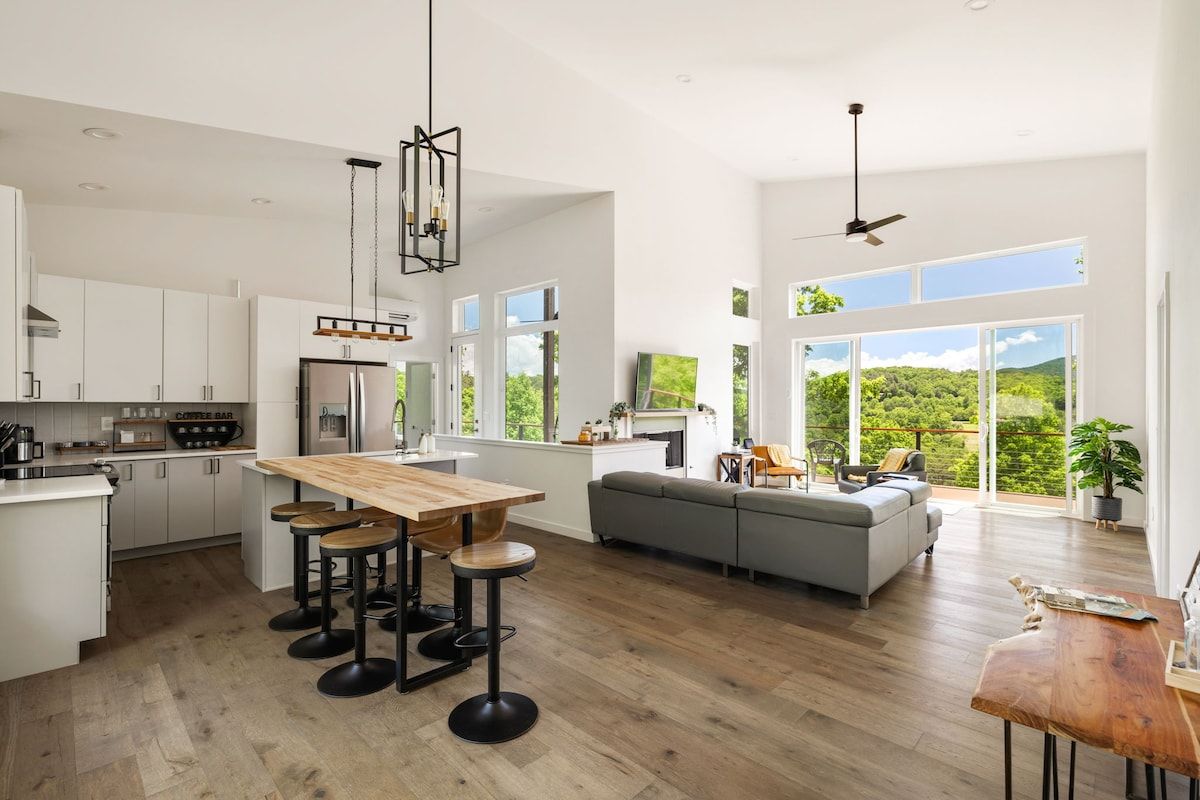 Cozinha moderna com ilha de madeira, banquetas e uma grande janela com vista para o verde.