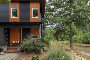 A modern two-story house with a dark exterior, wooden accents, and a front porch with seating. - Firefly Overlook | MTN Views + Chef's Kitchen (Young Harris)