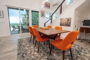 Ein Essbereich mit einem Holztisch und orangenen Stühlen, einer Treppe und einem großen Fenster mit Blick.