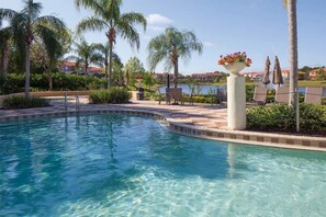 A clear swimming pool with a curved edge, surrounded by palm trees and lounge chairs. - 3BR Townhouse Near Disney Private Pool (Kissimmee)
