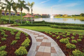 A landscaped pathway leading to a gazebo, a body of water, and a fountain. - 3BR Townhouse Near Disney Private Pool (Kissimmee)