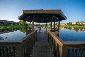 A wooden pier leading to a covered area with a view of a calm body of water and greenery. - 3BR Townhouse Near Disney Private Pool (Kissimmee)