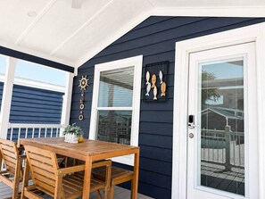 A wooden table and chairs on a porch with a dark blue exterior wall, white trim, and decorative fish wall art. - Villa Orca at Club Ballena (La Parguera)