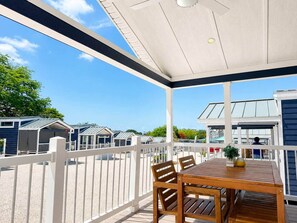 A covered outdoor area with a wooden table and chairs, a white fence, and a view of mobile homes in the background. - Villa Orca at Club Ballena (La Parguera)