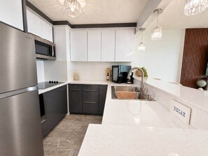 A modern kitchen with stainless steel appliances, white cabinetry, and a 'RELAX' sign on the countertop. - Wake Up to Ocean Views | Dos Marinas (Fajardo)