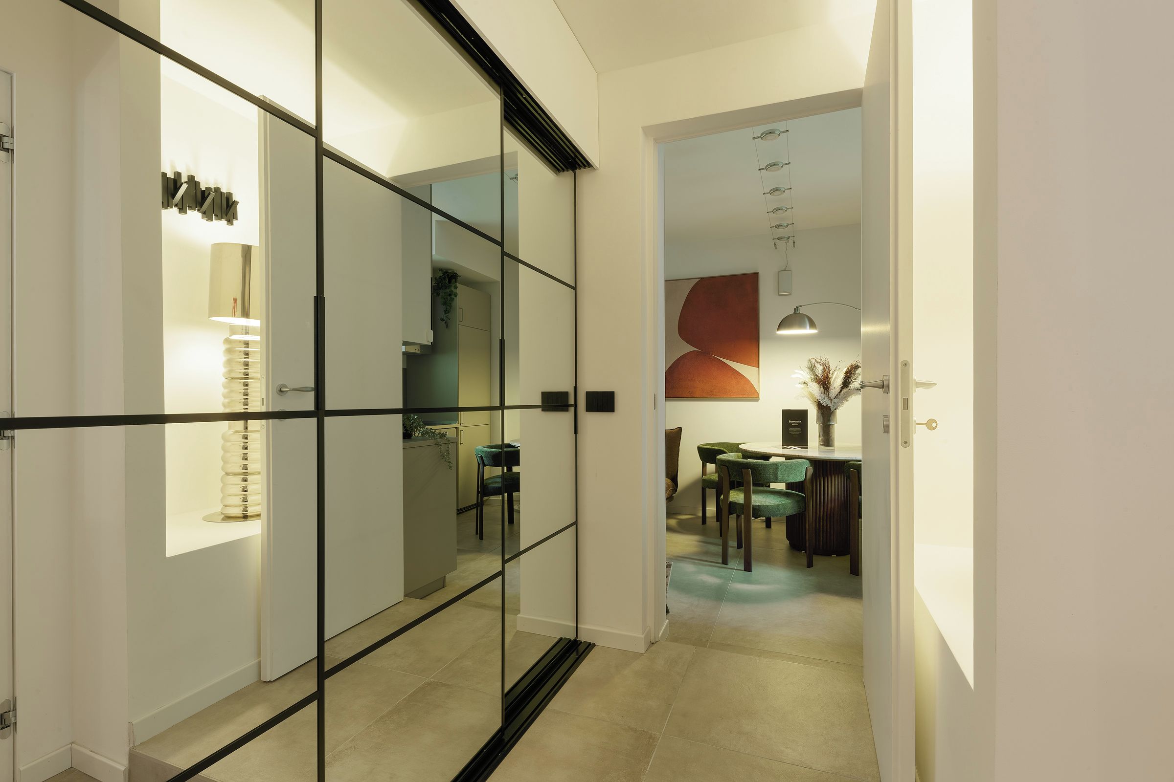 A modern interior with a glass partition, a dining area with a table and chairs, and a kitchen area with cabinets and a countertop.