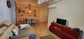A living room with a sofa, a television on a red stand, and a kitchen in the background. - Sunset Vibes Durrës – Modern Coastal Escape with Breathtaking Views, family frie (Durrës)