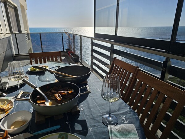 Ein Esstisch mit Blick aufs Meer, eine Pfanne mit Essen und ein Weinglas.