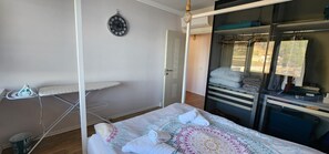 A bedroom with a bed, an ironing board, a wardrobe, and a clock on the wall. - Sunset Vibes Durrës – Modern Coastal Escape with Breathtaking Views, family frie (Durrës)