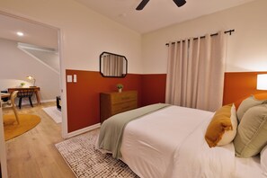 Un dormitorio con cama, mesita de noche, espejo, ventana con cortinas y escritorio con silla.