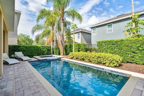 A swimming pool with lounge chairs and a hot tub, surrounded by greenery and a building. - 5BR Near Disney Private Pool, spa & Game Room (Kissimmee)