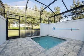 A swimming pool with a glass enclosure, surrounded by a paved deck and a white wall. - 3BR Townhouse Near Disney Pool & Mickey Room (Clermont)