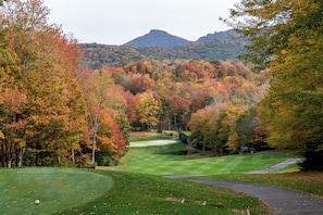 A golf course with a pond, surrounded by autumn-colored trees and a mountain in the background. - Large Sugar Mountain Home with Fireplace and Covered Deck (Sugar Mountain)