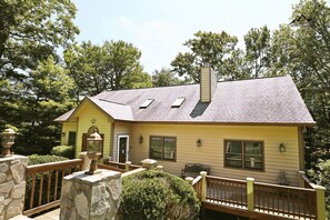 A yellow house with a stone deck, a chimney, and a stone wall. - Large Sugar Mountain Home with Fireplace and Covered Deck (Sugar Mountain)