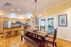 A spacious kitchen with wooden cabinets, a central island, and a dining area with a wooden table and chairs. - Large Sugar Mountain Home with Fireplace and Covered Deck (Sugar Mountain)