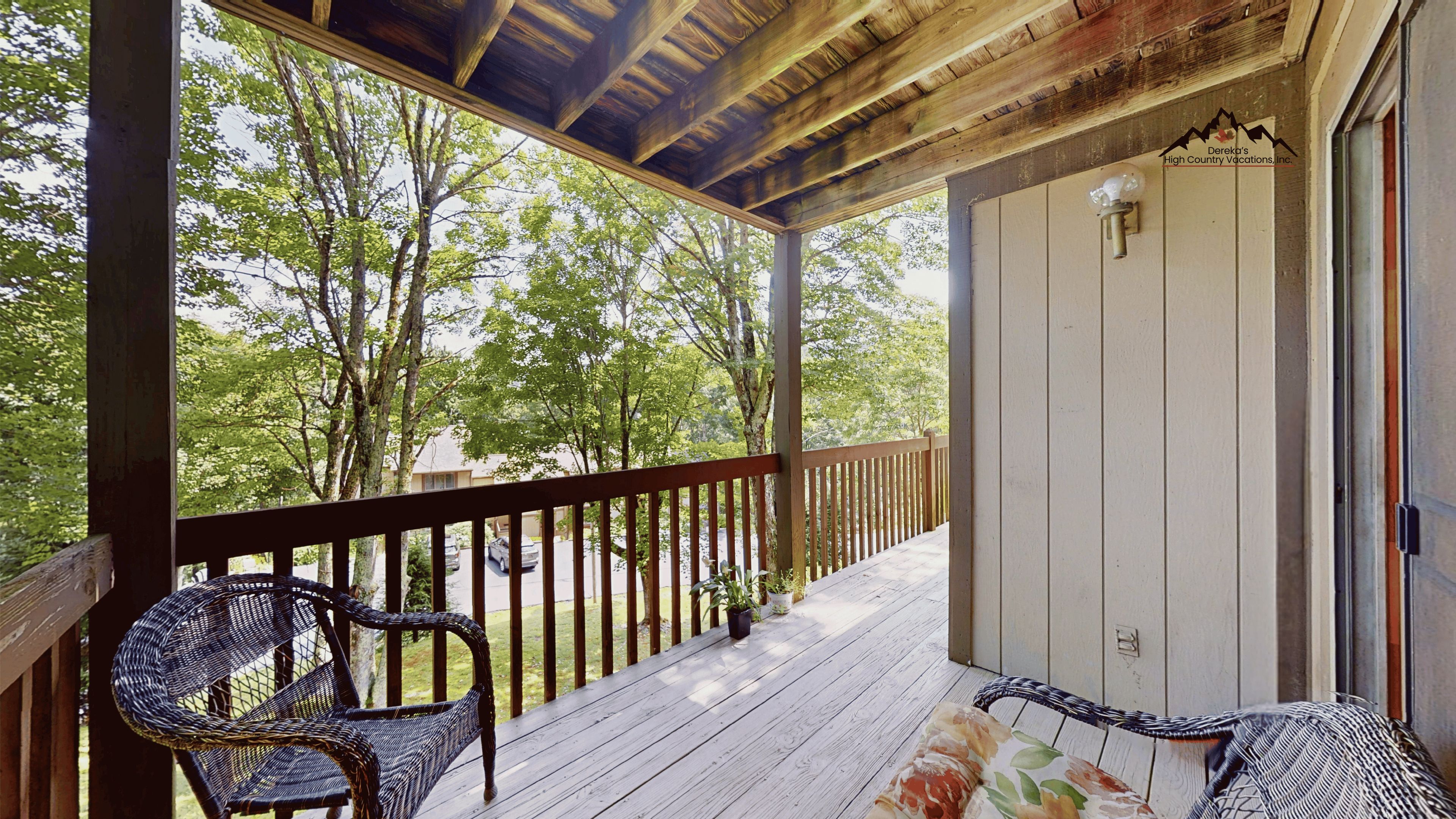 A covered porch with a wooden railing, a wicker chair, and a potted plant.