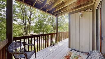 A covered porch with a wooden railing, a wicker chair, and a potted plant.