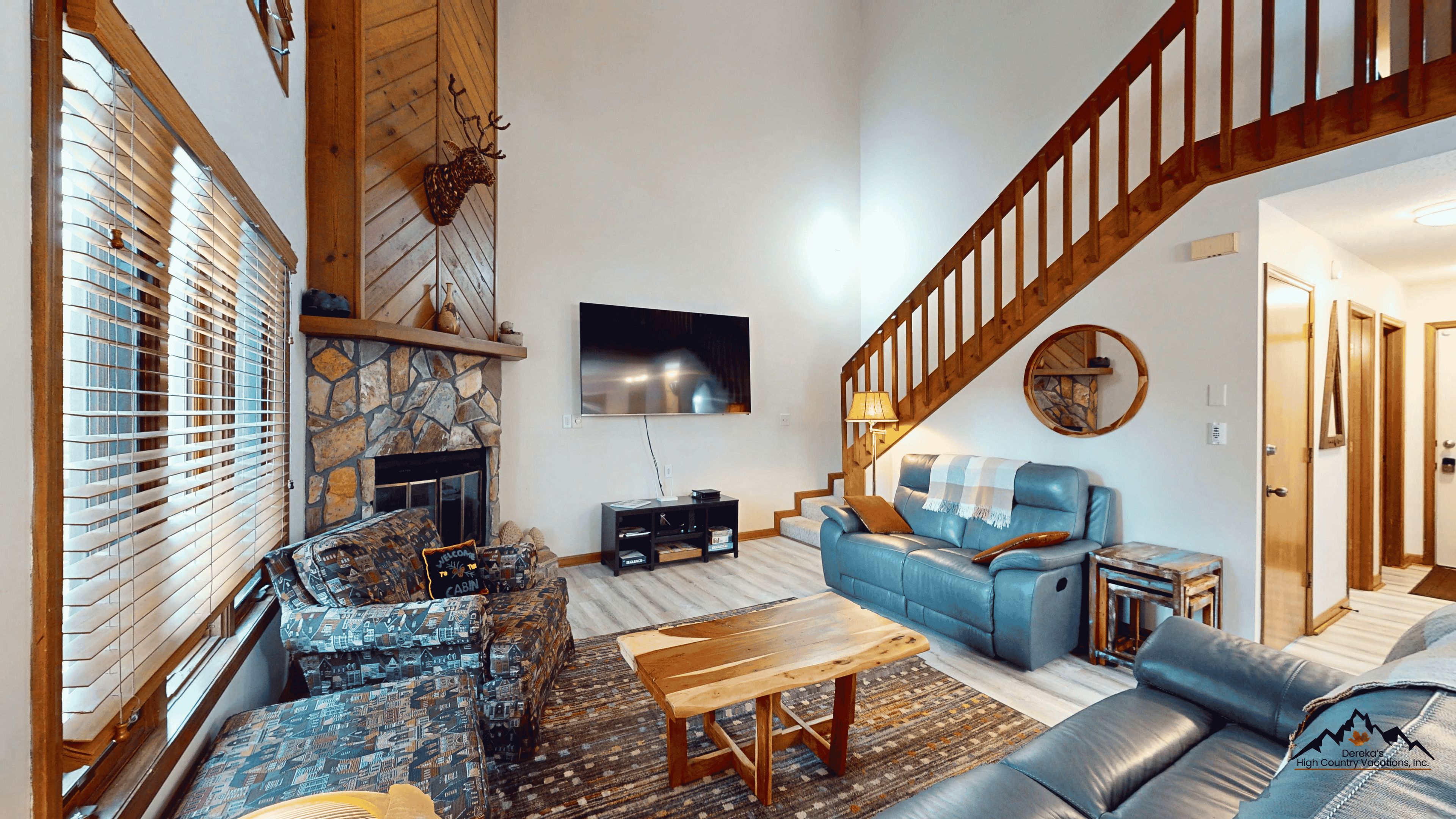 A living room with a stone fireplace, a blue sofa, a wooden coffee table, and a staircase.