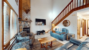 A living room with a stone fireplace, a blue sofa, a wooden coffee table, and a staircase. - Sweetspot in Chestnut Ridge (Sugar Mountain)