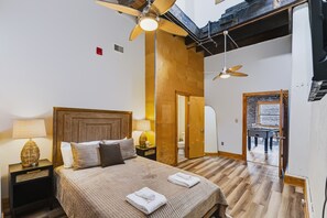 Ein Schlafzimmer mit einem hölzernen Bett, zwei Nachttischen, einem Deckenventilator und einer Tür zu einem weiteren Raum.