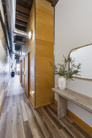 Un couloir avec un plancher en bois, un banc agrémenté d’un pot de fleurs et un miroir fixé au mur.