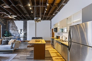 Une cuisine moderne dotée d’un îlot central, d’appareils électroménagers en acier inoxydable et de poutres apparentes en bois.