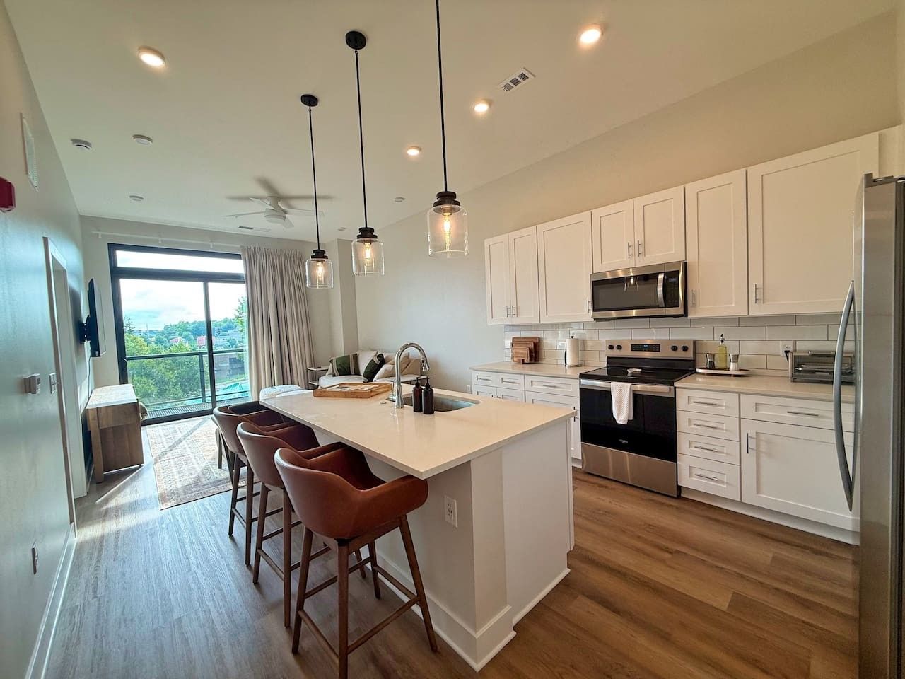A modern kitchen with a central island, bar stools, and a view of the outdoors.