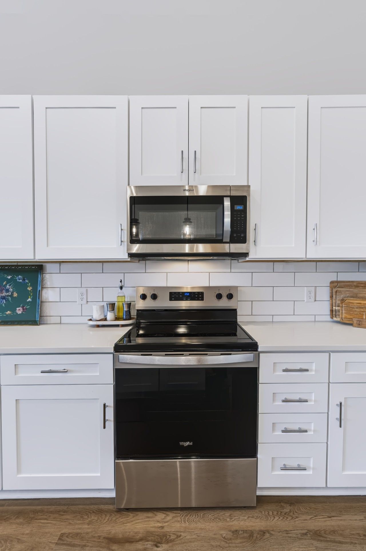 A kitchen with white cabinetry, a stainless steel microwave, and an oven.