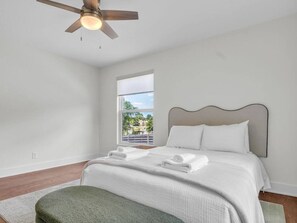 Ein Schlafzimmer mit Bett, Fenster, Deckenventilator und Blick ins Freie.