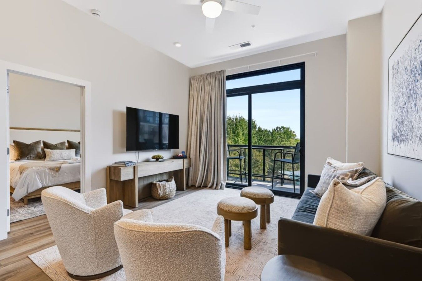 A modern hotel room with a bed, a TV, a balcony, and a seating area.